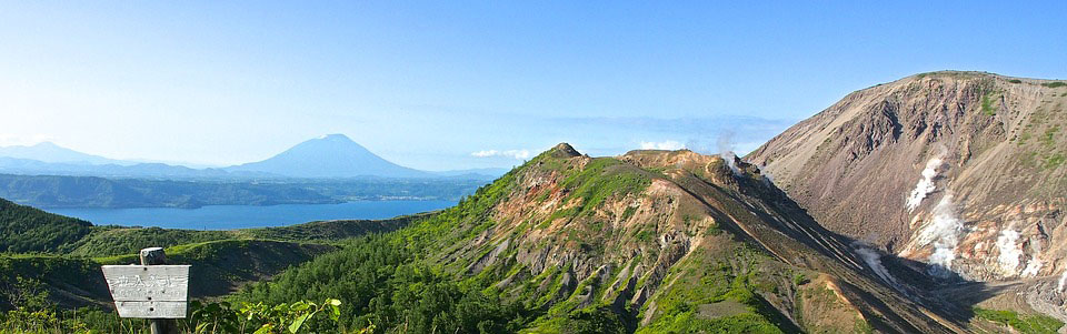 Two tree-covered mountains stand in the foreground, with more mountains and a lake visible but obscured by clouds in the background. 